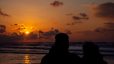 日落时站在海边的男人和女人的剪影